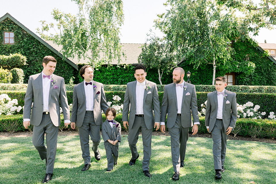 groom in a gray suit with white shirt and bow tie, with a matching white pocket square and the groomsmen in purple bow ties