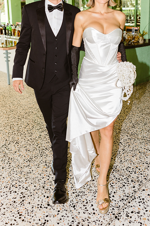 A chic wedding editorial featuring a bride in a pearl-detailed gown with black gloves and a groom in a black tuxedo.