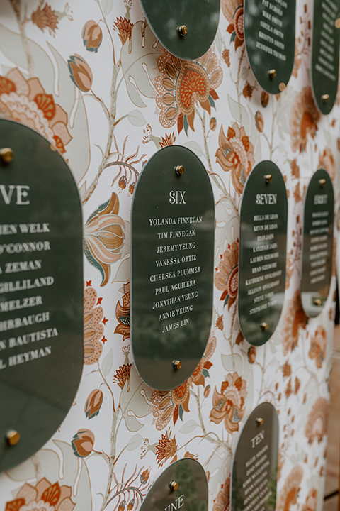Charming rustic boho wedding details, including hand-lettered signage and a beautifully designed seating chart, surrounded by greenery and wooden accents