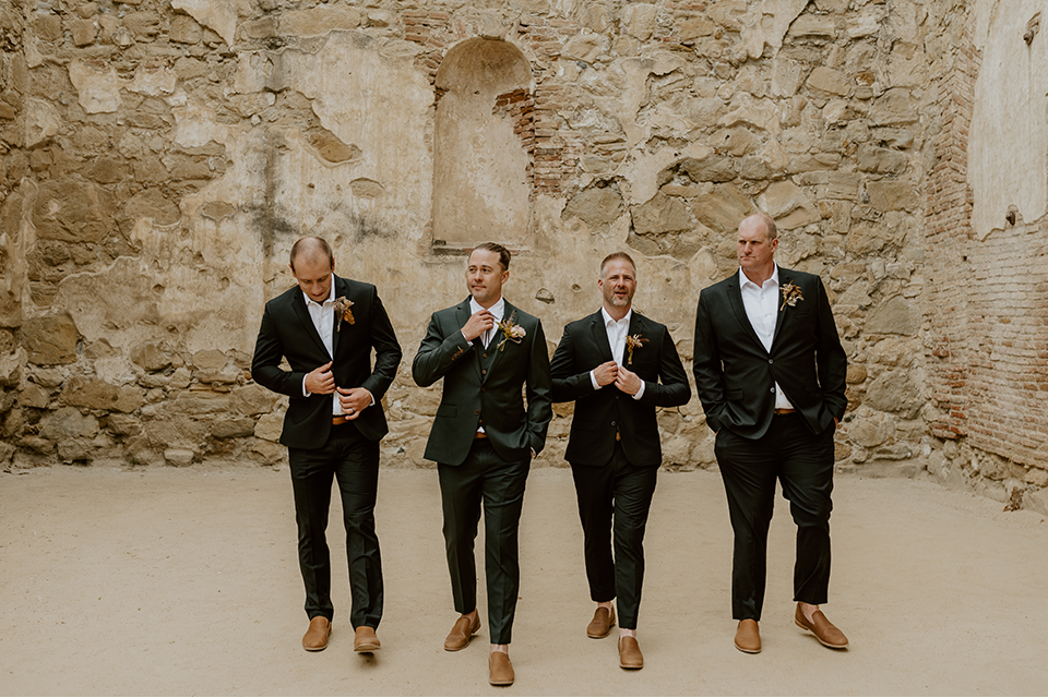 Groomsmen in matching green suits laughing and celebrating with the groom at an outdoor wedding