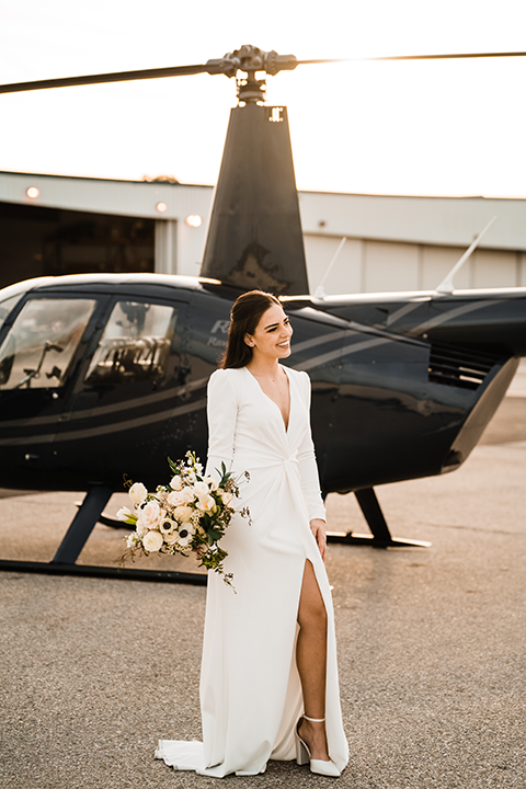 Bride stands in front of a private plane, her long dark waves cascading down her back as she gazes into the distance