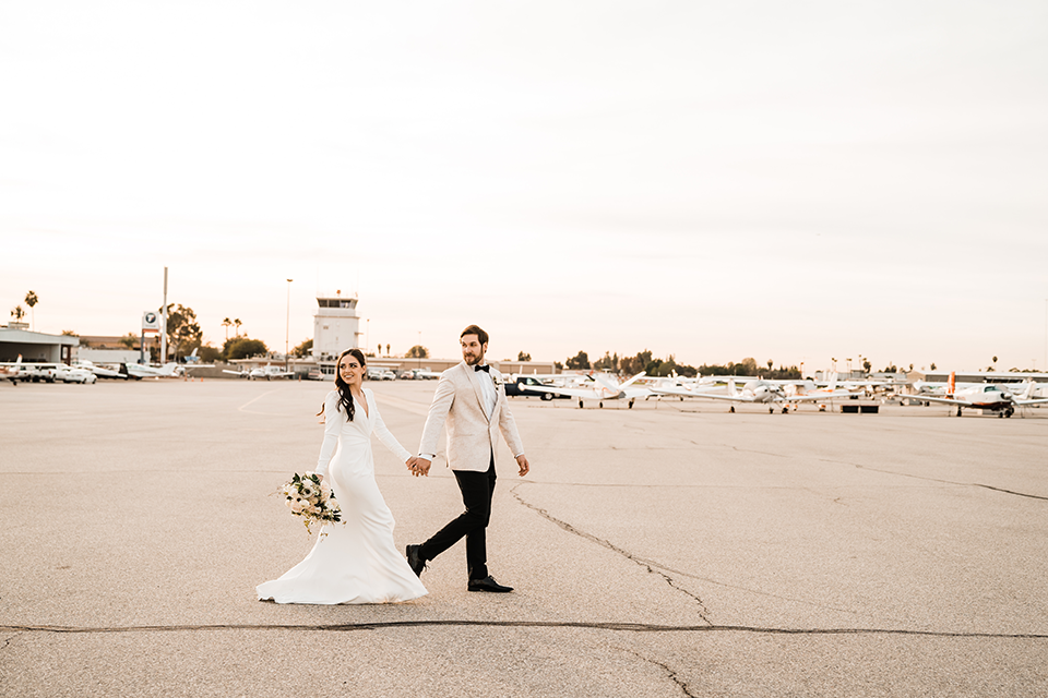 Bride and groom share a romantic moment on the runway at Hangar 21, with golden-hour lighting and a stunning white rose bouquet.