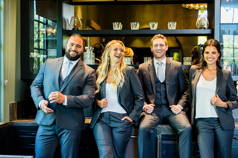 A group of people at a wedding party in gray suits smiling at the camera