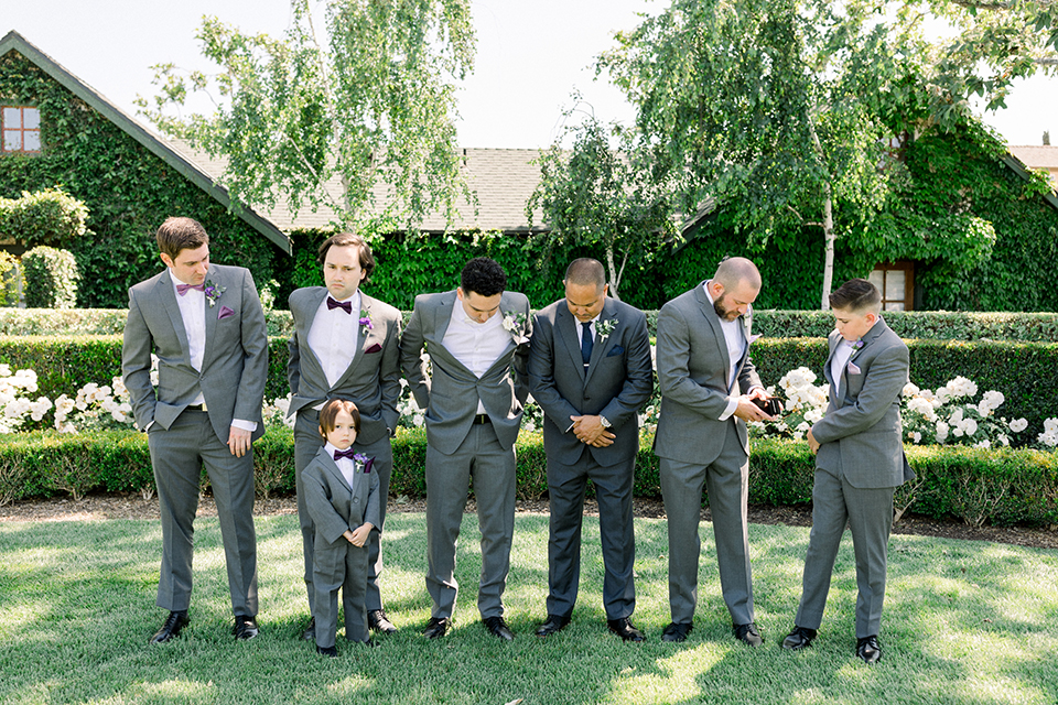 groom in a gray suit with white shirt and bow tie, with a matching white pocket square and the groomsmen in purple bow ties