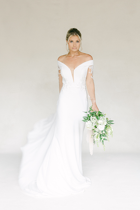 Bride in an off-the-shoulder wedding gown holding a white floral bouquet.