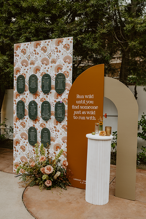 Charming rustic boho wedding details, including hand-lettered signage and a beautifully designed seating chart, surrounded by greenery and wooden accents