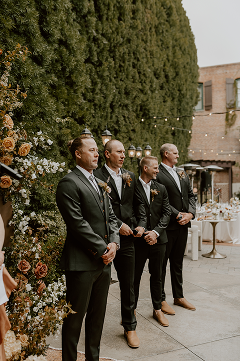 Groomsmen in matching green suits laughing and celebrating with the groom at an outdoor wedding