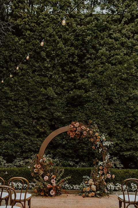 eautiful rustic boho wedding ceremony arch adorned with florals, greenery, and draped fabric, set against a natural outdoor backdrop